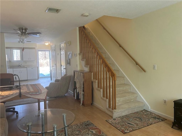 stairs featuring hardwood / wood-style flooring, sink, a textured ceiling, and ceiling fan