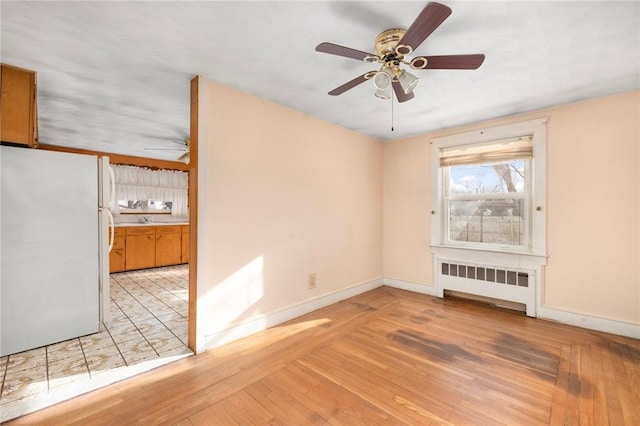 spare room with light wood-type flooring, radiator, and ceiling fan