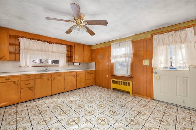 kitchen featuring ceiling fan, wood walls, radiator heating unit, and sink