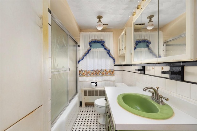 full bathroom with radiator, combined bath / shower with glass door, toilet, vanity, and tile walls