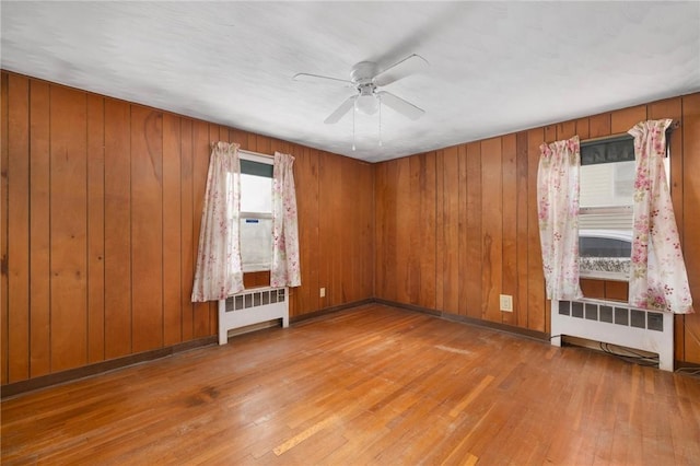 empty room featuring wooden walls, ceiling fan, wood-type flooring, and radiator