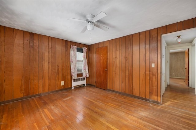 empty room with wooden walls, ceiling fan, light wood-type flooring, and radiator