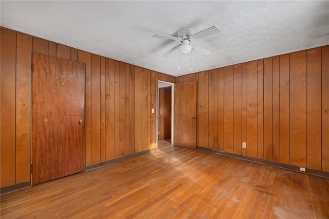 unfurnished room with light hardwood / wood-style flooring, ceiling fan, and wooden walls