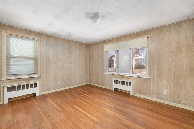 unfurnished living room featuring radiator heating unit, hardwood / wood-style flooring, and wooden walls