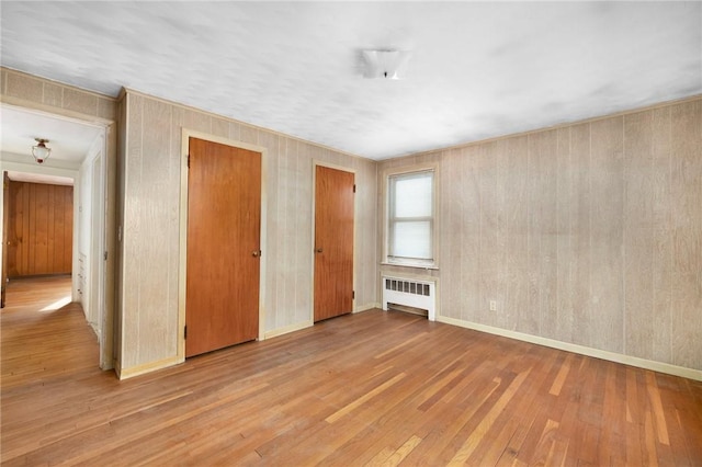 unfurnished bedroom with light wood-type flooring, radiator heating unit, and two closets