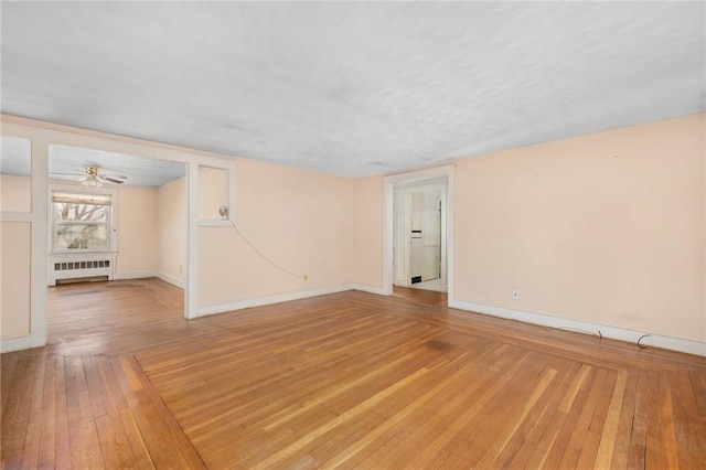 empty room featuring wood-type flooring, radiator, and ceiling fan