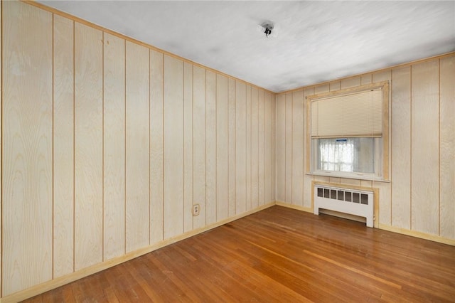 empty room with wood walls, radiator heating unit, and hardwood / wood-style floors