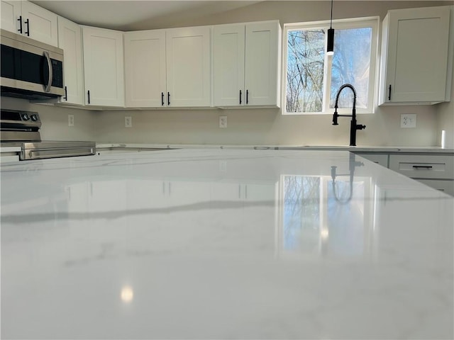 kitchen featuring white cabinets, stove, pendant lighting, and sink