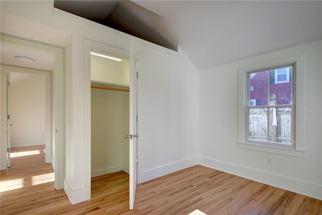 unfurnished bedroom with vaulted ceiling, a closet, and light wood-type flooring