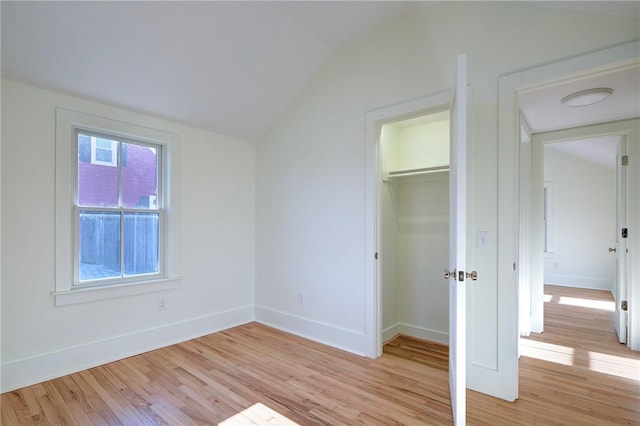 unfurnished bedroom featuring light hardwood / wood-style flooring, a closet, a spacious closet, and lofted ceiling