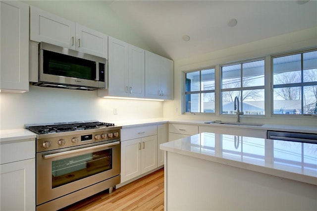 kitchen with white cabinets, appliances with stainless steel finishes, sink, vaulted ceiling, and light hardwood / wood-style flooring