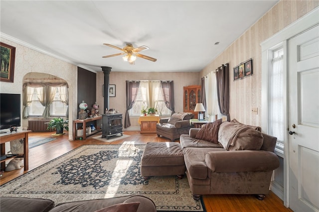 living room featuring a wood stove, ceiling fan, radiator heating unit, and light wood-type flooring