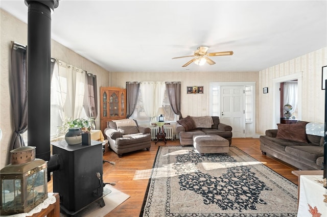 living room with light hardwood / wood-style floors, a wood stove, radiator, and ceiling fan