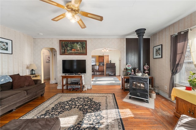 living room featuring hardwood / wood-style flooring, a wood stove, ceiling fan, and crown molding