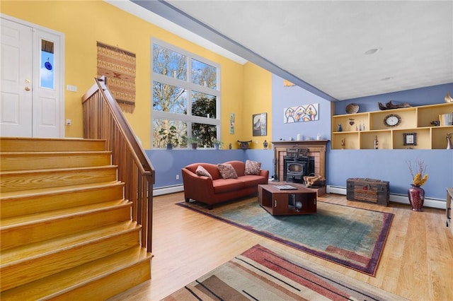 living room with wood-type flooring, a wood stove, and a baseboard heating unit