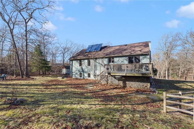 back of property with a wooden deck, a yard, and solar panels