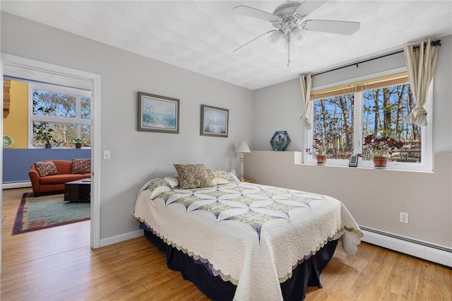 bedroom with multiple windows, light hardwood / wood-style floors, ceiling fan, and a baseboard heating unit