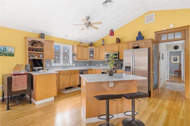 kitchen with appliances with stainless steel finishes, light wood-type flooring, backsplash, ceiling fan, and a center island