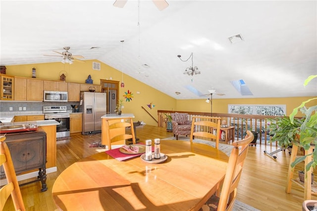 dining area featuring vaulted ceiling with skylight, ceiling fan, and light wood-type flooring