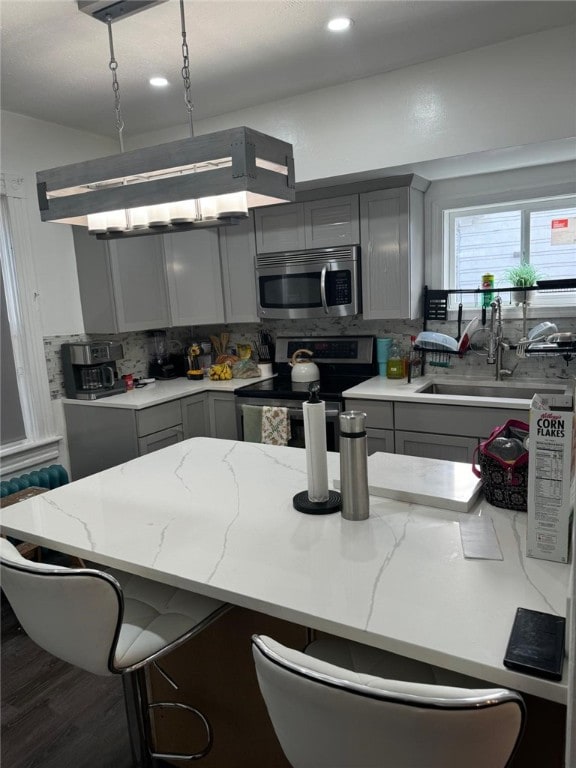 kitchen with a breakfast bar area, gray cabinetry, sink, and stainless steel appliances