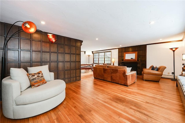 living room with light hardwood / wood-style floors, wood walls, a baseboard heating unit, a large fireplace, and ornamental molding