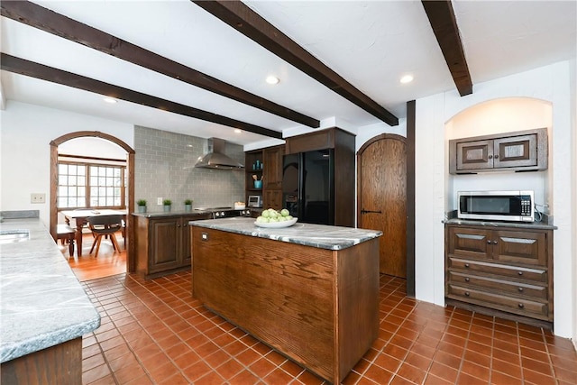 kitchen featuring backsplash, a center island, black refrigerator with ice dispenser, light stone countertops, and wall chimney range hood