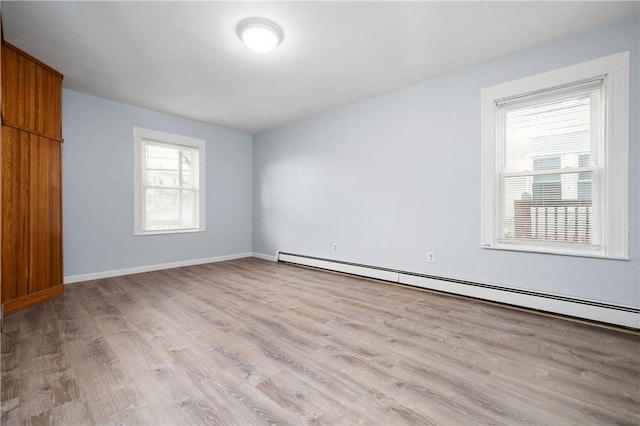 spare room featuring baseboard heating and light hardwood / wood-style floors