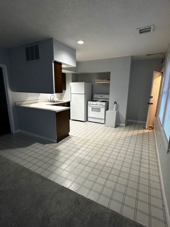 kitchen with kitchen peninsula, dark brown cabinets, white appliances, a textured ceiling, and sink