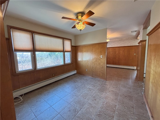 empty room featuring ceiling fan, wooden walls, and a baseboard heating unit