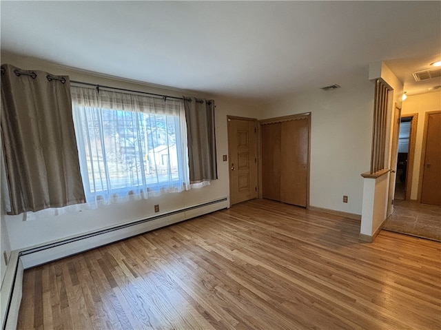 unfurnished bedroom featuring a closet, baseboard heating, and light hardwood / wood-style flooring