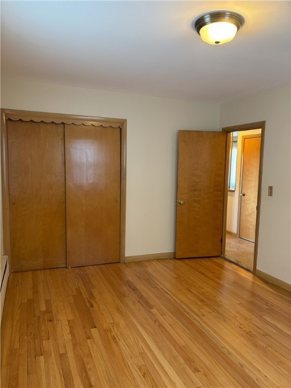 unfurnished bedroom featuring a closet, light hardwood / wood-style floors, and a baseboard radiator