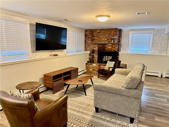 living room with hardwood / wood-style flooring, a brick fireplace, and a baseboard heating unit