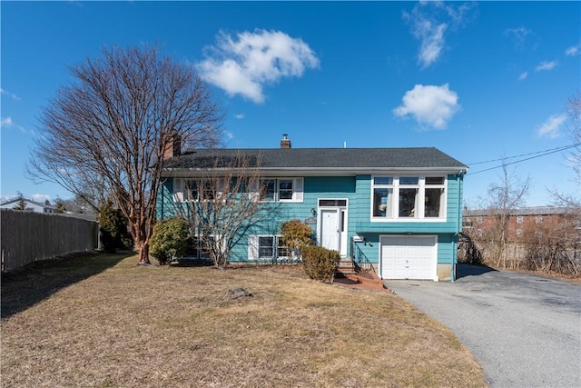 split foyer home featuring a garage, driveway, a front lawn, and fence