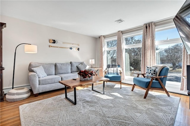 living room featuring visible vents, baseboard heating, and wood finished floors