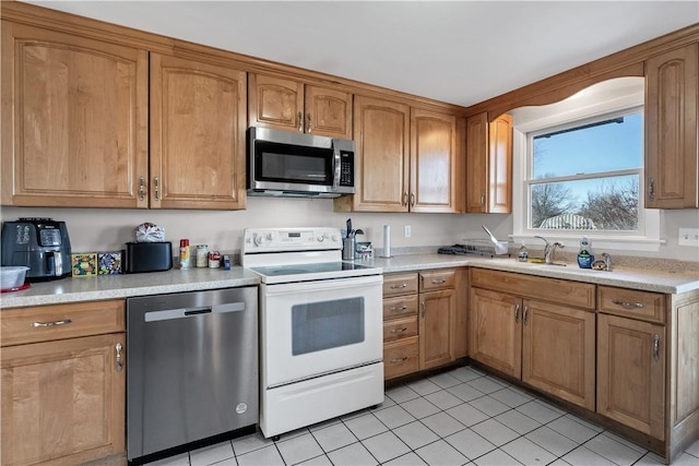 kitchen with light tile patterned flooring, stainless steel appliances, a sink, light countertops, and brown cabinetry