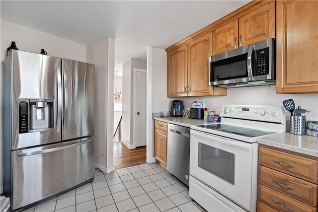 kitchen featuring light tile patterned flooring, baseboards, light countertops, appliances with stainless steel finishes, and brown cabinetry