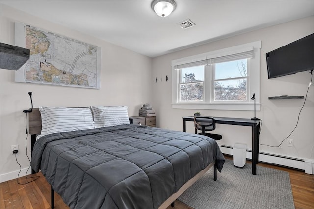 bedroom featuring a baseboard heating unit, visible vents, baseboards, and wood finished floors