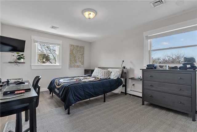 bedroom featuring a baseboard heating unit, wood finished floors, visible vents, and baseboards