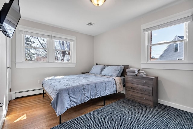 bedroom with a baseboard heating unit, visible vents, baseboards, and wood finished floors