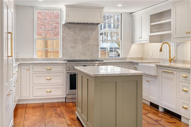 kitchen featuring premium range hood, stainless steel range, sink, a center island, and light hardwood / wood-style floors