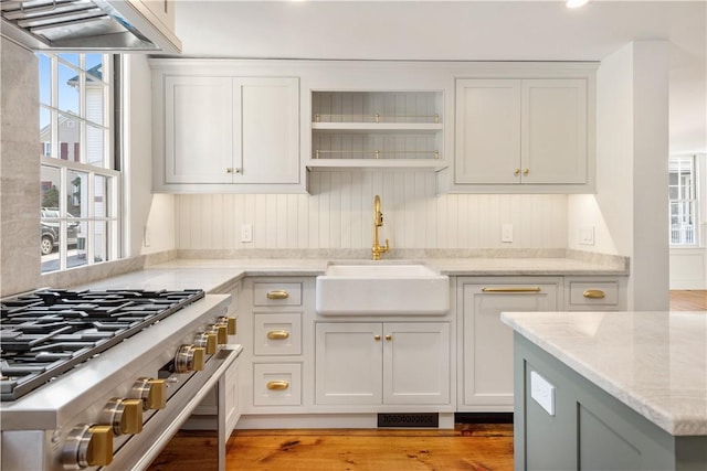 kitchen featuring sink, light hardwood / wood-style flooring, stainless steel range, light stone counters, and extractor fan