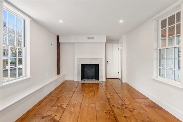 unfurnished living room with hardwood / wood-style flooring, a wealth of natural light, and a high end fireplace