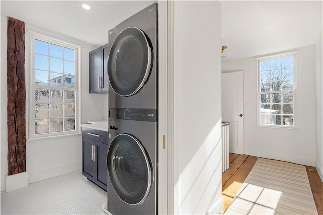 laundry area with stacked washer and dryer, cabinets, plenty of natural light, and light wood-type flooring