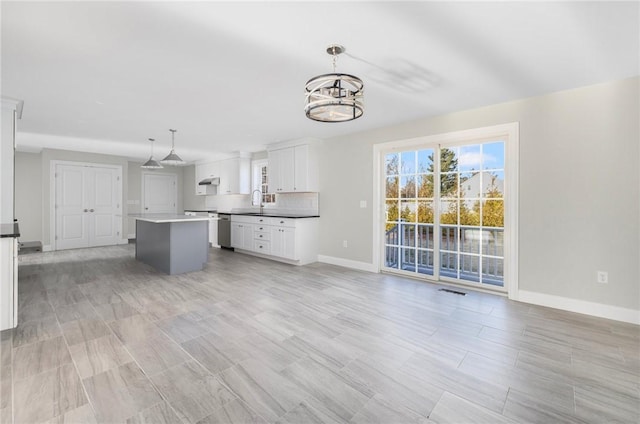 kitchen featuring pendant lighting, white cabinets, stainless steel dishwasher, decorative backsplash, and a kitchen island