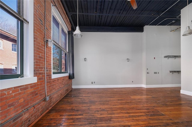 empty room featuring ceiling fan, dark hardwood / wood-style floors, a wealth of natural light, and brick wall