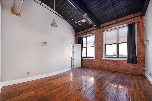 empty room with hardwood / wood-style floors, beam ceiling, ceiling fan, and brick wall