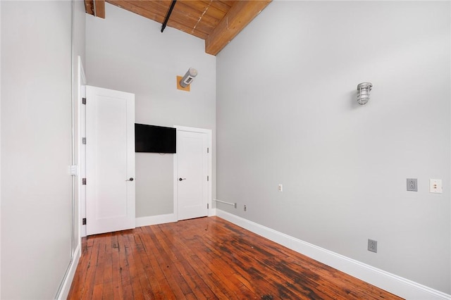 empty room with hardwood / wood-style floors, beam ceiling, a high ceiling, and wood ceiling