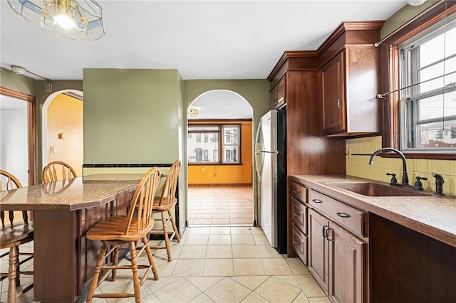 kitchen with a breakfast bar, sink, stainless steel fridge, light tile patterned floors, and tasteful backsplash