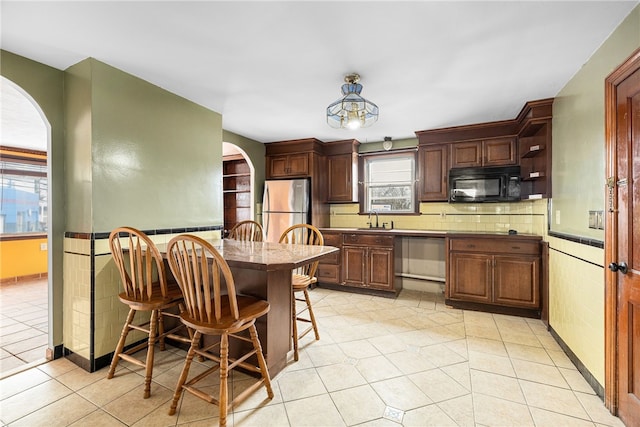 kitchen with decorative backsplash, appliances with stainless steel finishes, a kitchen breakfast bar, sink, and light tile patterned flooring