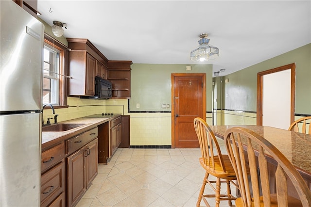 kitchen featuring pendant lighting, black appliances, sink, tile walls, and light tile patterned flooring